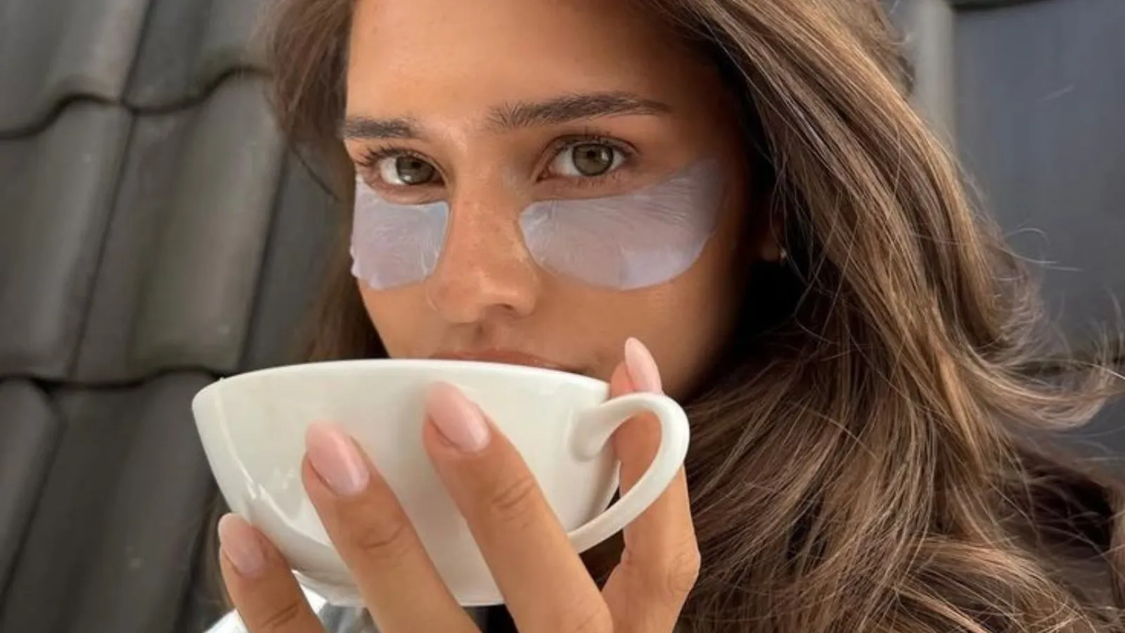 woman holding a cup of coffee and wearing eye patches
