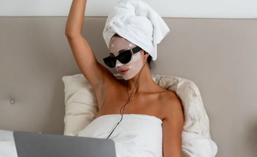woman with a collagen mask in bed looking in her laptop