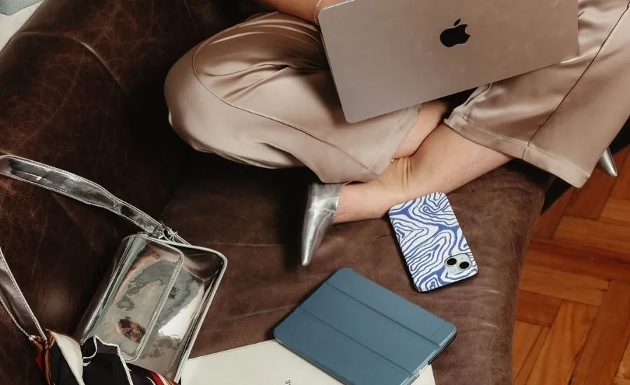 woman sitting on couch with her laptop on feet and a tablet and a phone next to her
