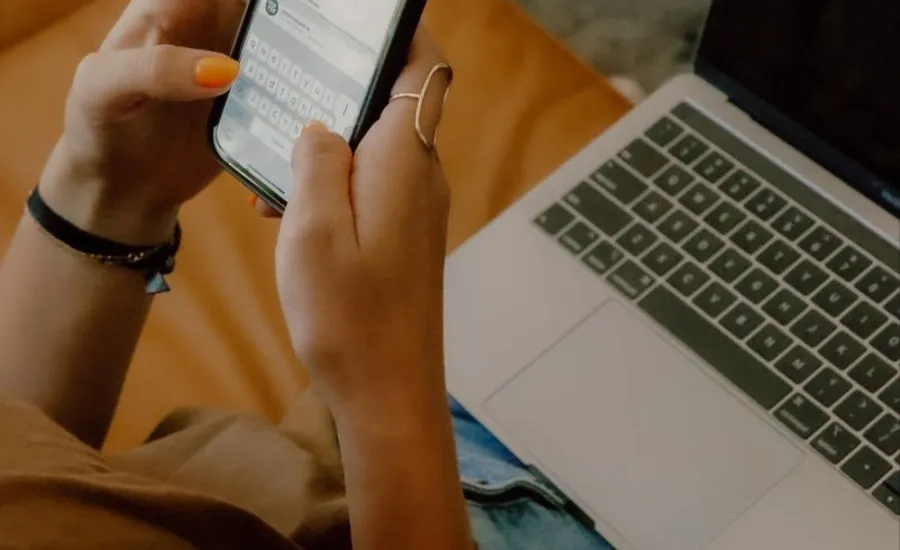 a woman holding her phone texting with the laptop on her laps