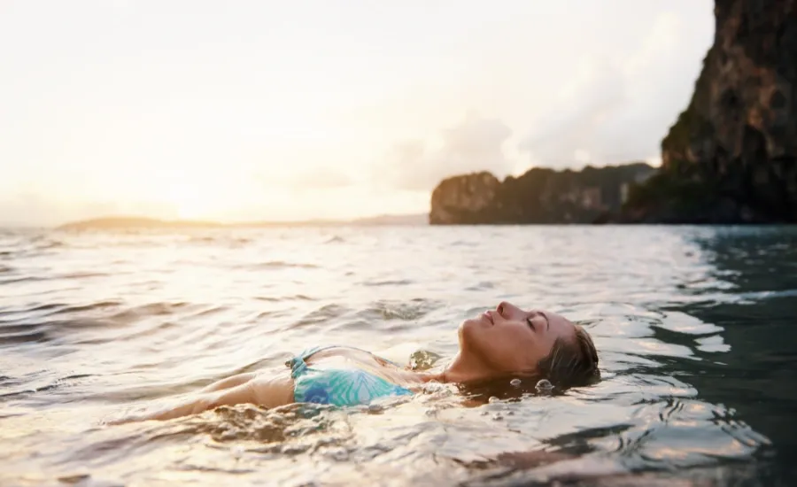 woman floating in the sea at sunset reseting her nervous system
